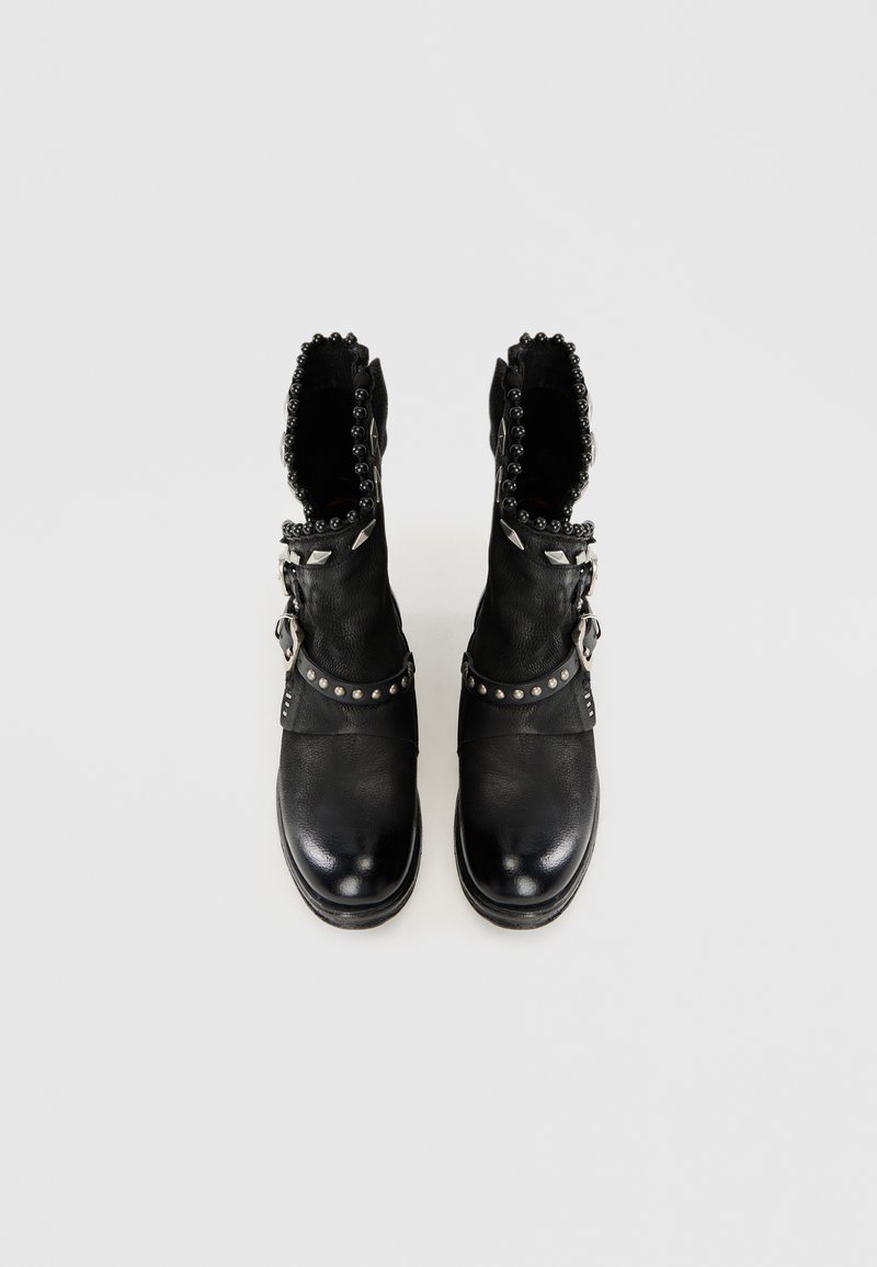 Schwarze Leder-Stiefelknöchel mit strukturierter Oberfläche, dekorativen Nieten, einer Schnallen-Detail und einem gewellten Rand am Kragen.