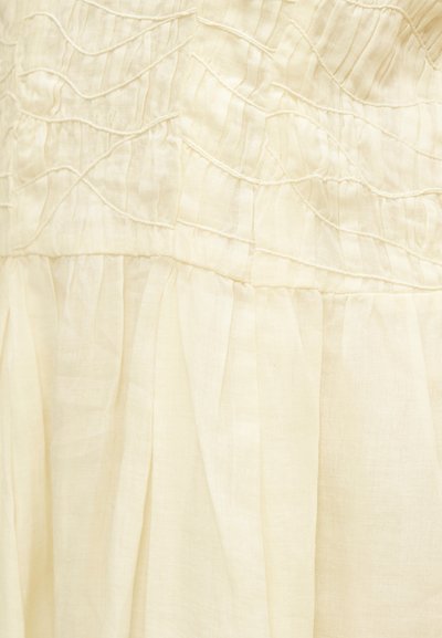 Κοντινή λήψη κρεμ υφάσματος με συγκεντρωμένες πιέτες και ραμμένα οριζόντια κυματιστά μοτίβα σε ελαφρύ υφαντό.