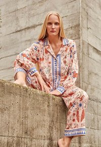 Floral-patterned, pale pink pajama set with blue accents, featuring long sleeves, a collar, and relaxed fit. Soft, lightweight fabric.