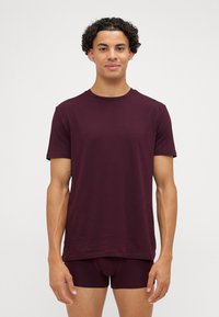 Burgundowa koszulka i bokserki, gładki materiał, dekolt typu crew neck, krótkie rękawy i dopasowany krój, noszone przez osobę na neutralnym tle.