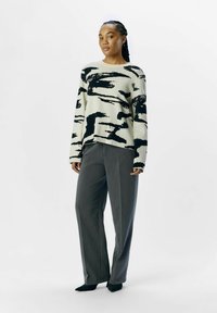 Sweater med sort abstrakt mønster på en cremefarvet baggrund, med lange ærmer og en afslappet pasform, parret med grå skræddersyede bukser.