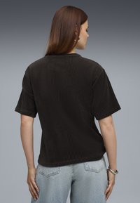 Zwarte corduroy t-shirt met korte mouwen, geribbelde textuur en een relaxed fit. Draag het met lichtblauwe high-waisted jeans.