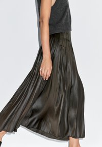 Gonna midi plissettata in satin verde oliva scuro, caratterizzata da un design fluido e una texture liscia, abbinata a un top grigio senza maniche aderente.