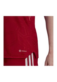 Rotes Sporttrikot mit strukturiertem geometrischem Muster, Aeroready-Branding und leicht geschwunghem Saum. Mit weißen Streifenakzenten.