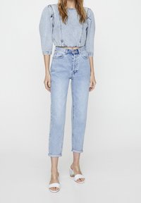 Top corto de mezclilla azul claro con mangas abullonadas, combinado con jeans de tiro alto azul claro. Zapatos de tacón abiertos en color blanco.