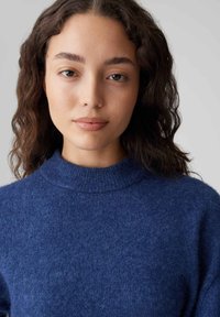 Maglione in maglia blu navy con collo alto, realizzato in tessuto morbido e testurizzato, caratterizzato da una vestibilità rilassata e sottili variazioni di colore.