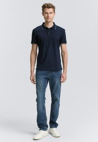 Een marineblauw poloshirt met een contrasterende witte kraagafwerking, gecombineerd met lichtblauwe jeans en witte sneakers. Ontworpen met een klassieke pasvorm en korte mouwen.