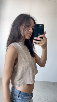 Top de tanque cropped em bege claro com um acabamento texturado, combinado com jeans de ganga azuis. O top apresenta braçadeiras largas e um decote redondo.