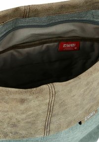 Bolsa de tela verde con una parte superior de cuero marrón. El interior presenta un forro suave y una etiqueta roja con la marca "ZWEI". Diseño simple y práctico.