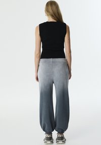 Zwart mouwloos topje gecombineerd met lichtgrijze, ombre wijd-uitlopende broek. De broek heeft een geribde taille en elastische boorden, wat zorgt voor een ontspannen pasvorm.
