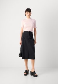 Helles rosa, geripptes Kurzarmoberteil, schwarze Midirock mit Taschen und klobigen schwarzen Plateau-Sandalen. Einfaches Design, glatte Texturen.