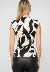 Top avvitato beige con motivi neri a foglia, maniche corte, texture a coste e scollatura a girocollo, abbinato a leggings neri aderenti.