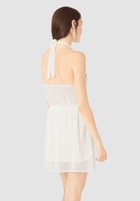 Vestido blanco con cuello halter, confeccionado en una tela ligera, que cuenta con una cintura elástica, un diseño fluido y un detalle de lazo en la parte posterior.