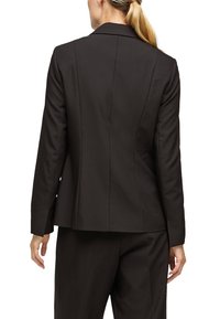 Blazer noir sur mesure avec une coupe structurée, doté d'une fente unique à l'arrière et d'une texture de tissu lisse. Se marie avec un pantalon assorti.