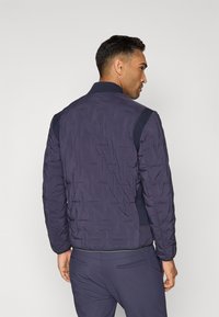 Veste bomber matelassée bleu marine avec un col côtelé et des panneaux latéraux, dotée d'une finition texturée et de poignets élastiques.