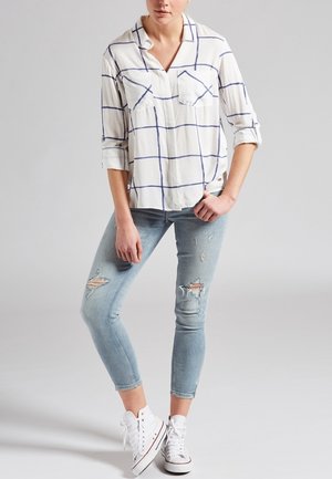 Camicia bianca a quadri a maniche lunghe con due tasche sul petto, abbinata a jeans skinny azzurri strappati e sneaker alte bianche.