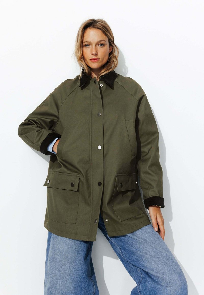 Veste vert olive avec un col en velours côtelé noir, des boutons-pression et deux poches avant ; coupe décontractée avec une texture lisse et des manches raglan.