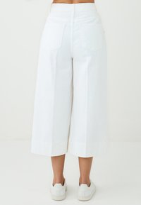 Pantaloni bianchi in cotone a gamba larga con vita alta, dotati di due tasche posteriori e orlo rifinito, abbinati a sneakers bianche.
