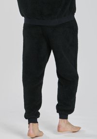 Flauschige schwarze Jogginghosen mit weichem Stoff. Merkmale sind elastische Bündchen und ein elastischer Bund. Das Bein hat einen lockeren Schnitt, ideal für Komfort.