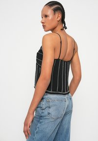 Czarny crop top w pionowe białe paski, z cienkimi ramiączkami i dopasowanym krojem. W zestawieniu z luźnymi, jasnoniebieskimi dżinsami.
