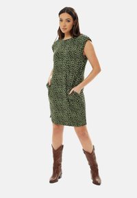 Green leopard print dress with short sleeves and side pockets, paired with brown cowboy boots. The fabric has a smooth texture.