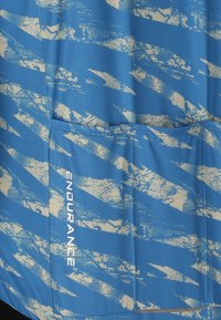 Tissu bleu texturé avec des motifs abstraits beiges et une poche portant le mot "ENDURANCE" en texte blanc vertical.