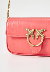 Coral pink handbag with crocodile texture, bronze bird embellishment, and a chain strap. Rectangular shape with flap closure.