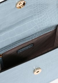 Lyseblå taske med krokodilleskindsprint, der har en åben klap, som viser det brune indre foring og guld magnetlukning.