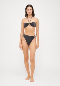 Juodas blizgus bikini su kaklo juostele ir aukštu juosmeniu. Abiejuose gaminiuose yra žiedų akcentai ir glotni tekstūra.