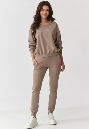 Beżowa bluza z długim rękawem i dopasowane dresy wykonane z miękkiego materiału. Bluza ma okrągły dekolt oraz ściśnięte mankiety; dresy mają tapered nogawki.