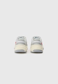 Sportschoenen met een grijze bovenkant, voorzien van lichtgrijze accenten, een crèmewitte tussenzool en rode details aan de zijkanten. Dikke rubberen zolen voor ondersteuning.