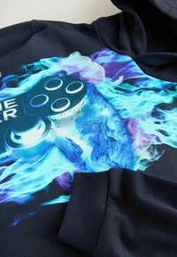 Kapuzensweatshirt in Navy mit einem lebendigen blau-lila Grafik eines Gamepads mit Flammenmotiven auf der Vorderseite.