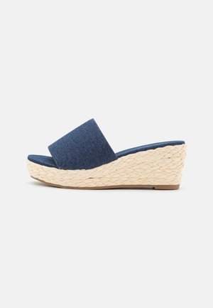Wedge sandal med flettet naturbund og bred mørkeblå stofrem, åben tå slip-on stil på en ensfarvet baggrund.