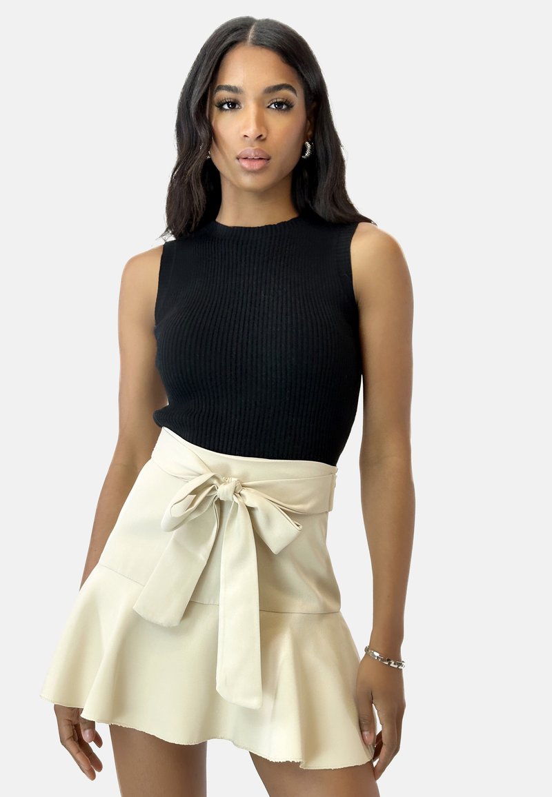 Top sin mangas de canalé negro combinado con una falda color crema clara que presenta una cintura con lazo atado y un dobladillo acampanado, creando un efecto de capas.