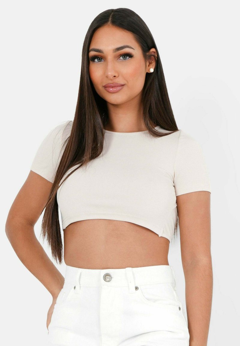 Top corto beige chiaro con maniche corte, texture a coste, scollatura rotonda, abbinato a pantaloni bianchi a vita alta.
