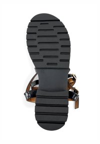 Zwarte rubberen sandaalzool met een getextureerd grip patroon en een ronde neus. Bevat dunne, glanzende banden en een gladde tan inlegzool. Maat 40.