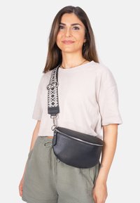 Schwarze Leder-Umhängetasche mit strukturiertem Oberflächendesign, runder Form und silbernem Reißverschluss. Verfügt über einen gemusterten verstellbaren Tragegurt.