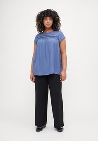 Blue short-sleeved blouse with smocking detail at the neckline, paired with black wide-leg trousers and black flats. Smooth fabric texture.