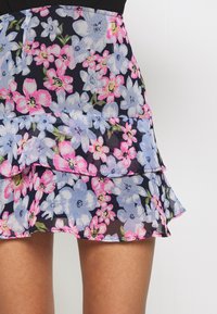 Jupe florale avec un fond bleu marine foncé orné de fleurs bleu clair et rose, avec des volants superposés et une texture transparente.