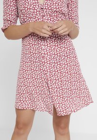 Rode bloemenjurk met knoopsluiting aan de voorkant, halve mouwen en een vloeiende zoom. Heeft een wit bloemenpatroon op een gestructureerde stof.