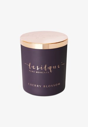 Fioletowy słoik świecy z błyszczącą złotą pokrywką. Posiada tłoczone napisy: "lesilque PURE MOMENTS" oraz "CHERRY BLOSSOM" w złotej czcionce.