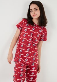 Röd pyjamasett med korta ärmar, prydd med ett upprepande mönster av hjärtan och tecknade figurer. Mjuk och lätt tyg.