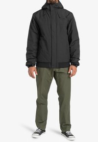 Sort isoleret jakke med hætte, elastiske manchetter og frontzipper. Sammen med olivengrønne bukser og sorte sneakers.