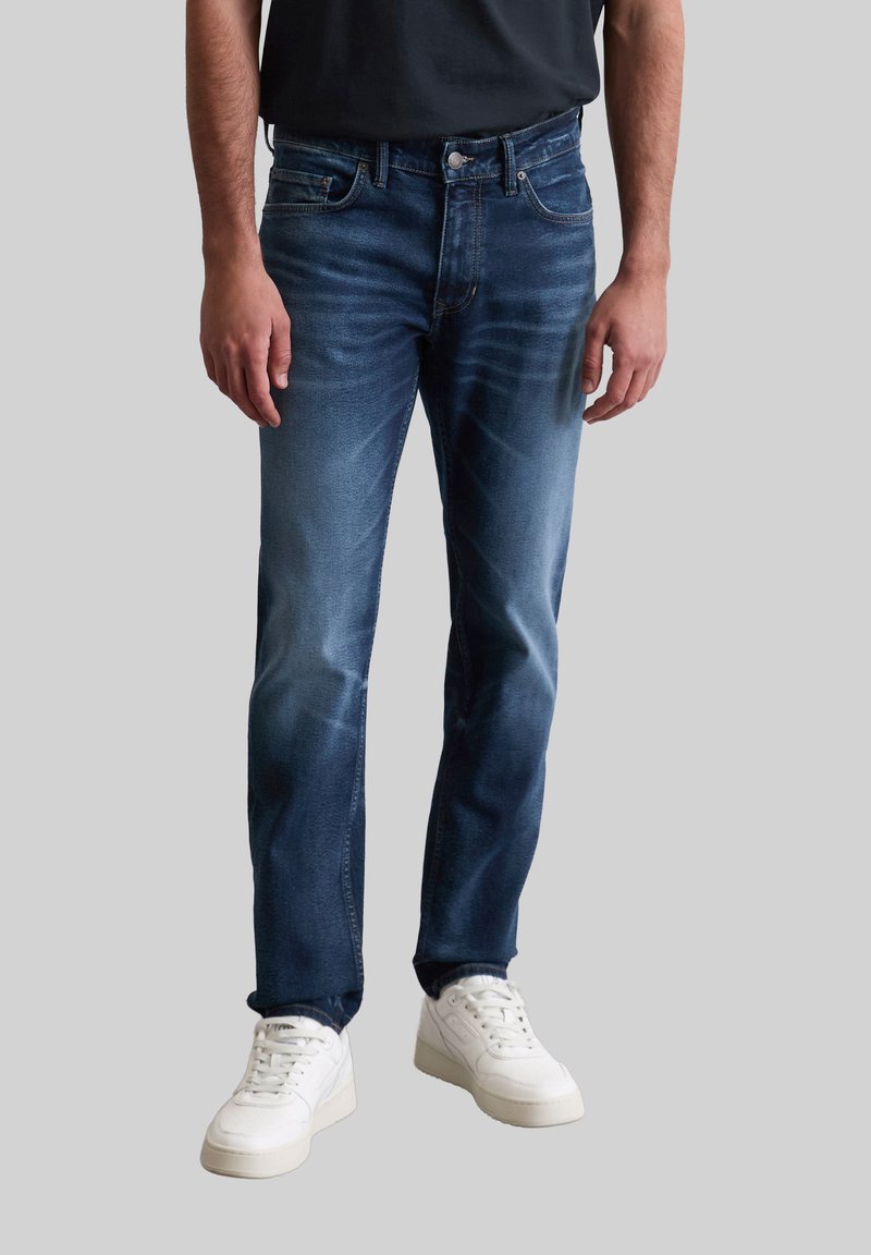 Blauwe denim jeans met een vervaagde wasservice, rechtachterig ontwerp, vijf zakken, met een knoop en rits sluiting, gecombineerd met witte sneakers.