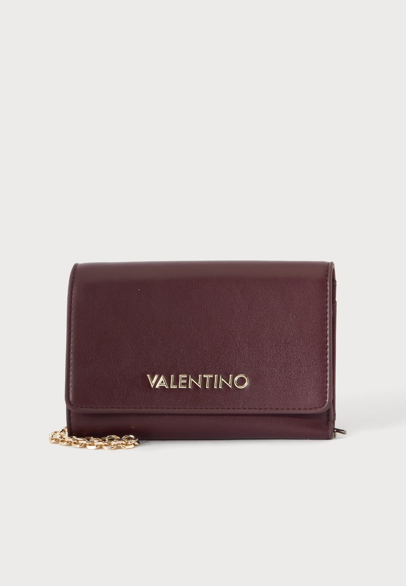 Виненочервена кожена чанта Valentino с златна верижка и златни букви с логото отпред, поставена на обикновен фон.