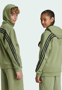 Sudaderas con capucha verdes, con rayas negras a lo largo de las mangas, textura suave, bolsillos tipo canguro, combinadas con pantalones cortos a juego.