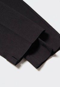 Pantalons en tissu noir avec une texture lisse et un design ajusté, présentant des plis bien pressés et un détail de revers plié.