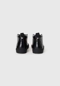 Black high-top sneakers featuring smooth leather, a textured sole, and a padded ankle. Silver hardware accents on the back.