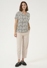 Top a maniche corte bianco e nero a motivo con scollatura a V, abbinato a pantaloni beige chiaro e mocassini neri spessi. Tessuto di una consistenza liscia.