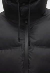 Μαύρο μπουφάν puffer με ψηλό γιακά, με λεία, γυαλιστερή υφή, εμπρόσθιο φερμουάρ και ρυθμιζόμενα κορδόνια στη κουκούλα.